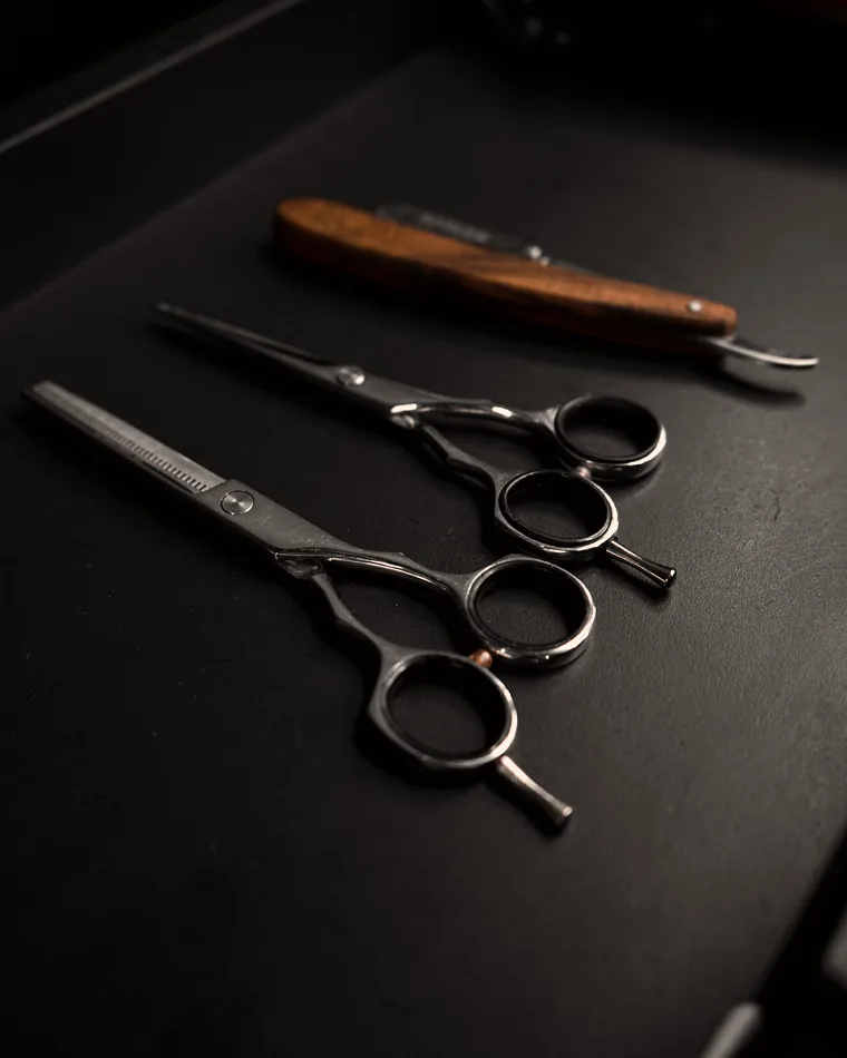 Rasoir droit et ciseaux de barbier posés sur un plan sombre
